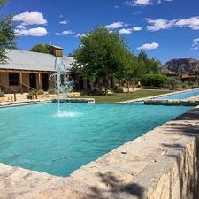 Fountain beside building and trees under blue sky.